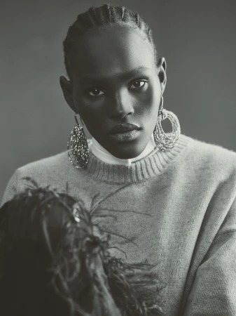 Close-up portrait of a Black woman with braided hair wearing a light sweater and statement earrings in a studio setting.