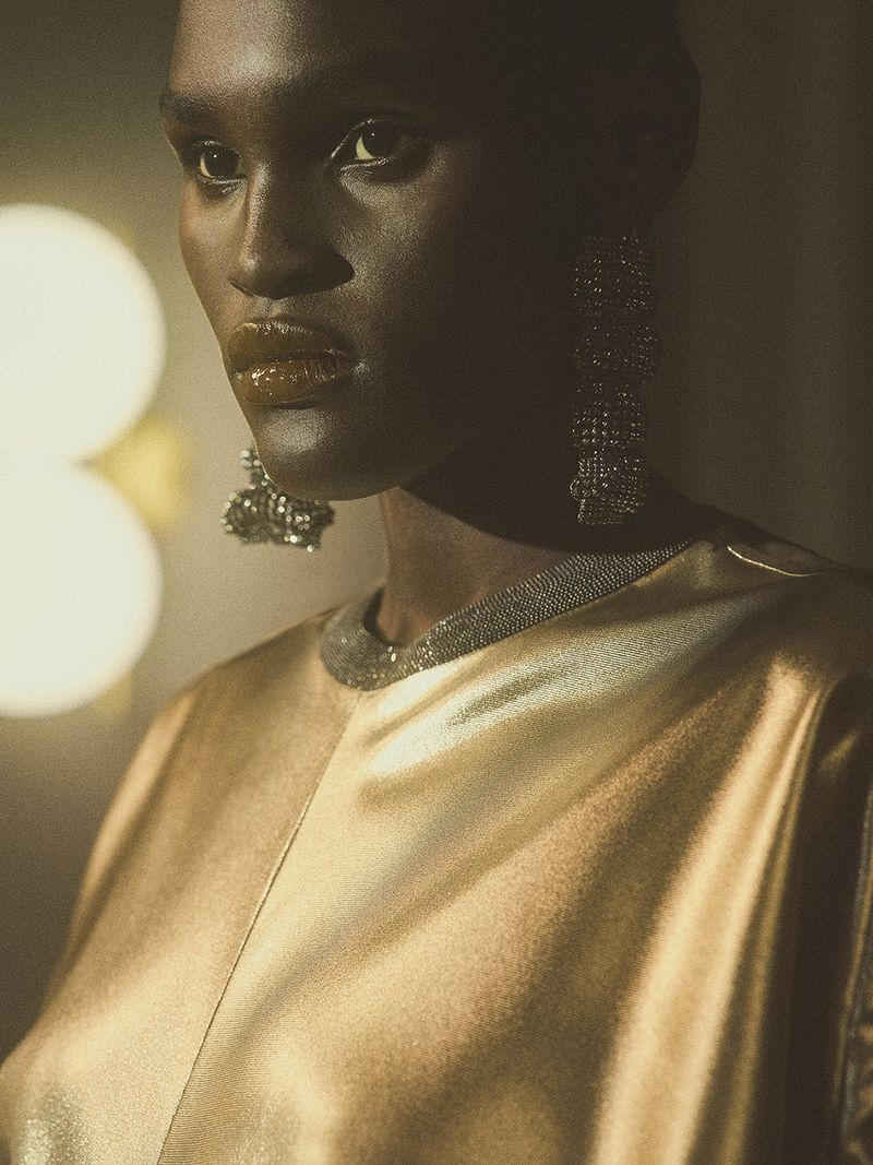 Close-up portrait of an African American woman with dark skin, wearing a gold top, and large earrings. Soft, diffused lighting.