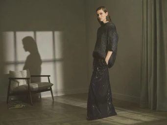 Model Luna Bijl wearing a dark textured knit top and sequined wide-leg trousers standing in a room with window shadows.