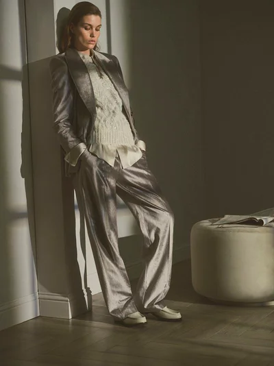 Model leaning against a wall wearing a grey suit and textured white top for Brunello Cucinelli