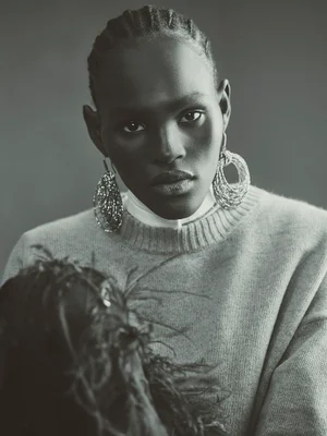 Black and white portrait of model Ageer Ayuen wearing a knit crewneck sweater and large sparkling statement drop earrings.