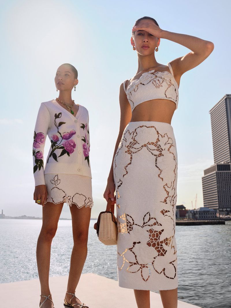 Two female models posing on a waterfront pier wearing floral embroidered white outfits for Oscar de la Renta.