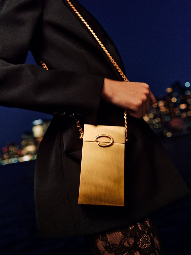 Close-up shot of a person holding a gold clutch with a gold chain strap in front of a dark background with city lights.