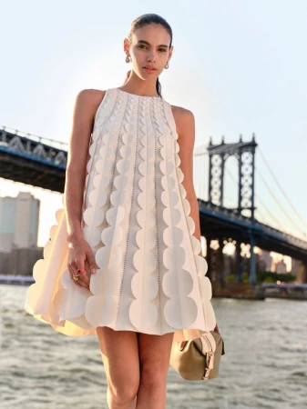 Fashion shoot of a woman wearing a cream-colored, above-the-knee dress with circular designs, posing in front of a bridge and river.