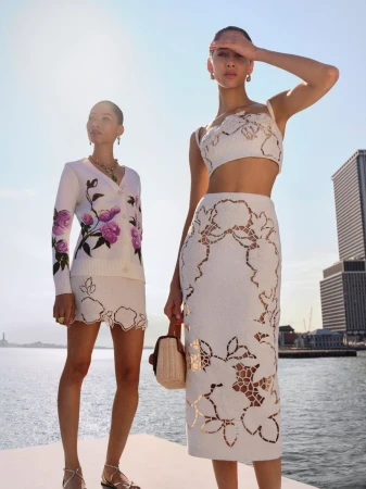 Two female models posing on a waterfront pier wearing floral embroidered white outfits for Oscar de la Renta.