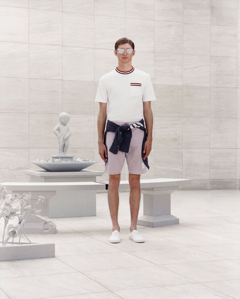 A slender adult male models casual fashion: white tee, striped shorts, white sneakers, and sunglasses, standing in a tiled indoor setting.