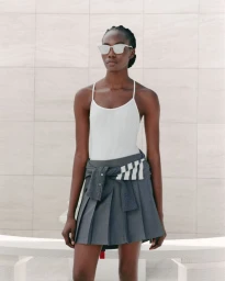 Model wearing white sunglasses, white tank top, and pleated grey skirt for Thom Browne S/S 24