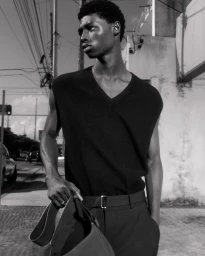 Monochrome portrait of model Zaram Obasi wearing a sleeveless black V-neck knit vest and belted trousers on a sunny street for COS.