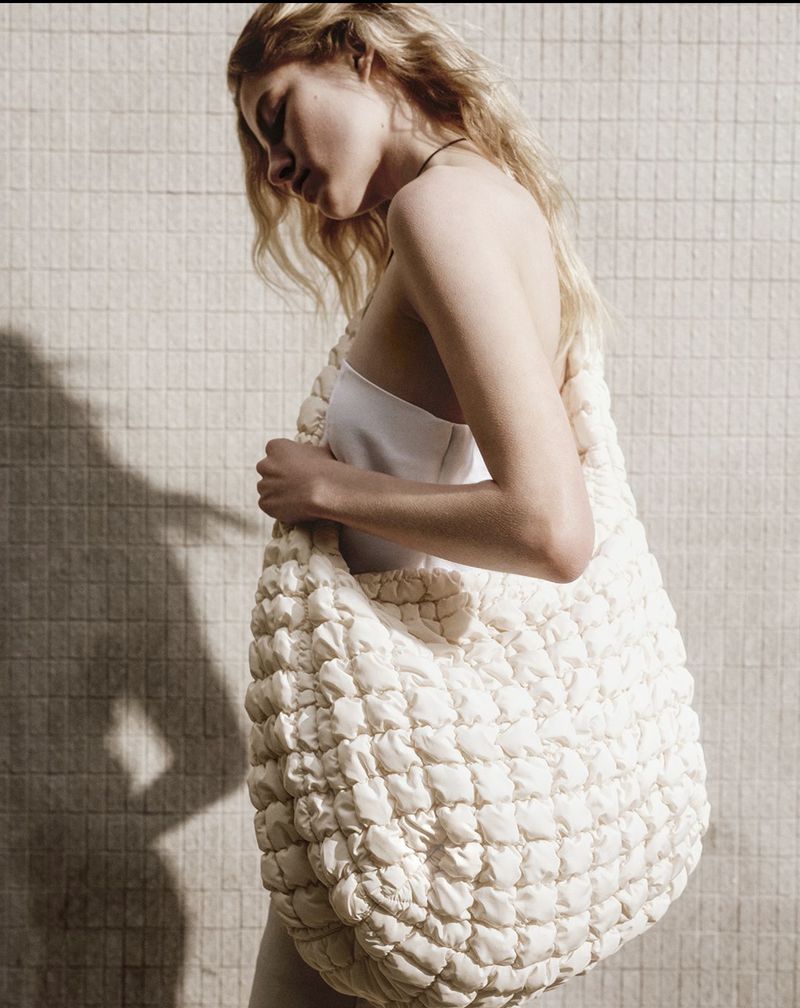 Model Felice Nova Noordhoff posing with an oversized cream quilted shoulder bag against a sunlit tiled wall.