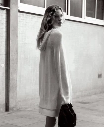 Model in hooded white sweater carrying a dark handbag outdoors against a tiled wall for COS Summer Newness.
