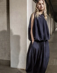 Felice Nova Noordhoff in a voluminous navy sleeveless maxi dress standing against a concrete pillar.