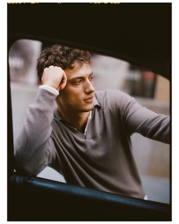 Handsome man with curly hair in gray sweater in a car with arm resting on the open car door. Automotive fashion lifestyle portrait.
