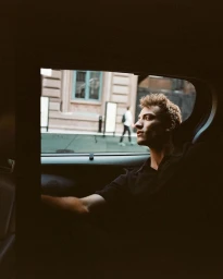 Model Serge Rigvava wearing a black polo shirt while looking out the window from the backseat of a car.