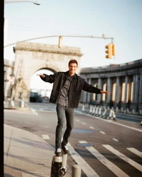 Model Serge Rigvava balances on a street bollard wearing a black jacket and jeans near an urban archway.