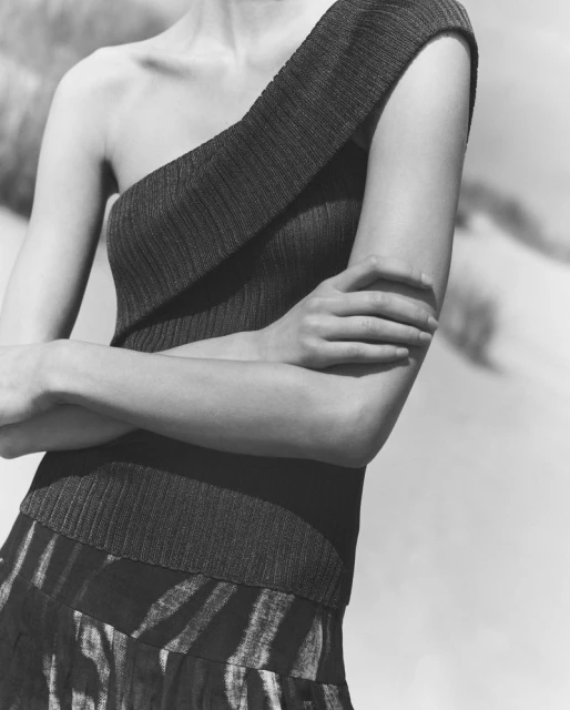 Monochrome fashion shot of a woman in a one-shoulder top and patterned skirt, posing with arms crossed against a neutral backdrop.
