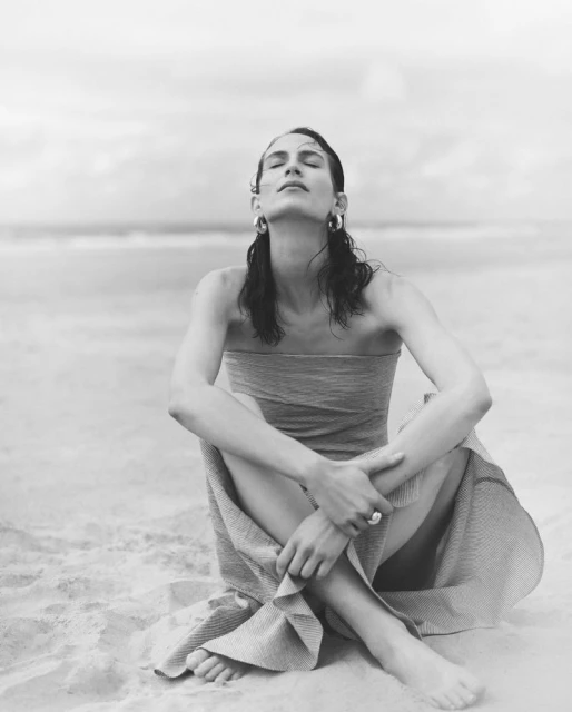 Monochrome portrait of a woman on a sandy beach with eyes closed, wrapped in fabric, exuding peacefulness and natural beauty.