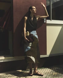 Woman in a black halter top and patterned midi skirt posing in sunlight against an exterior wall.