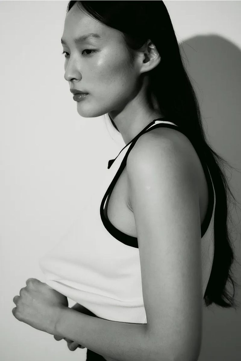 Monochrome portrait of an Asian female model in a tank top. Her dark hair contrasts with the light background and her fair skin.