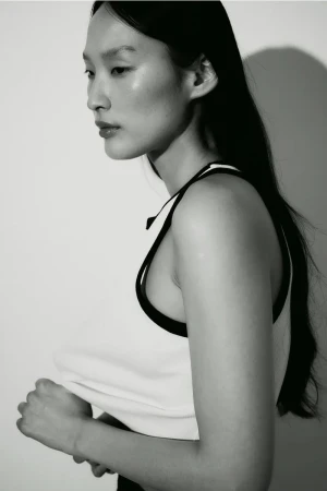 Monochrome portrait of an Asian female model in a tank top. Her dark hair contrasts with the light background and her fair skin.