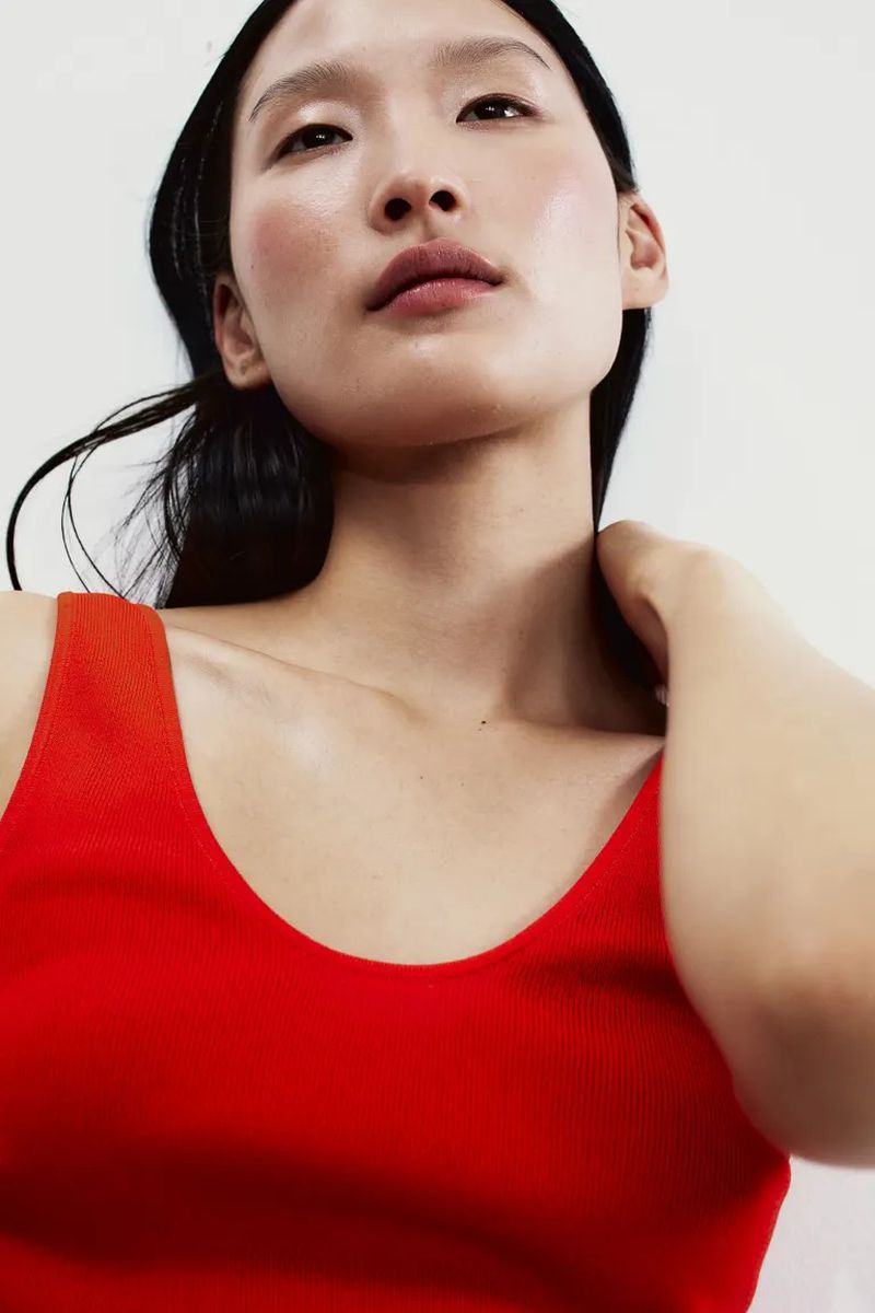 Close-up studio shot of a woman with fair skin wearing a red tank top, with dark hair, neutral expression, and soft, even lighting.