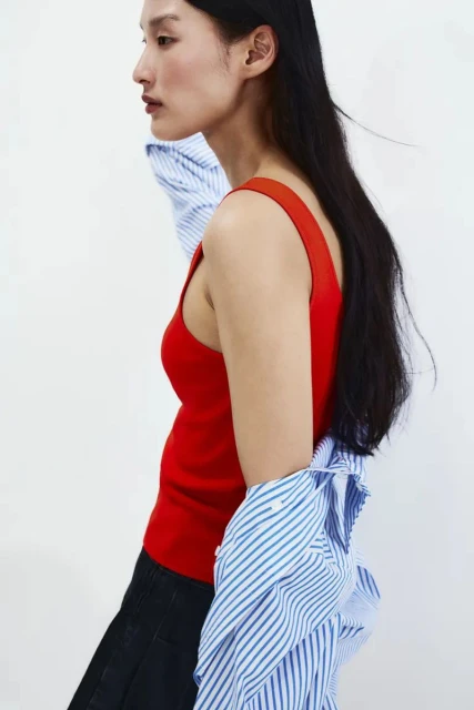 Woman in red tank top and blue striped shirt against a white background. Studio shot, fashion editorial, minimalist style, side view.