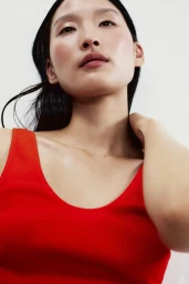 Close-up portrait of a woman wearing a vibrant red scoop-neck top against a plain white background.