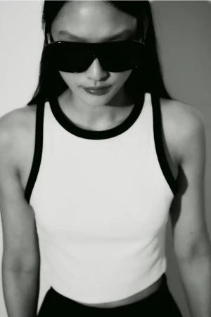 Model Yoonmi Sun wearing oversized black shield sunglasses and a white tank top with black contrast trim against a white backdrop.