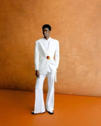 Model in a white suit with a round brooch against an orange textured studio backdrop for Orange Culture