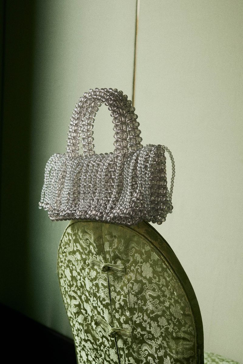 Elegant handbag crafted from translucent beads resting on a vintage chair with patterned upholstery, creating a sophisticated visual.