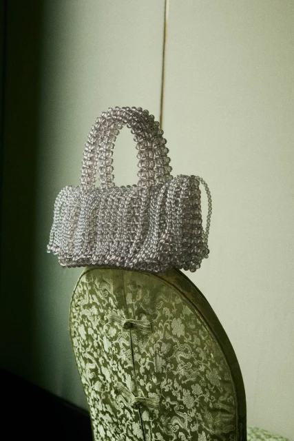 Elegant handbag crafted from translucent beads resting on a vintage chair with patterned upholstery, creating a sophisticated visual.