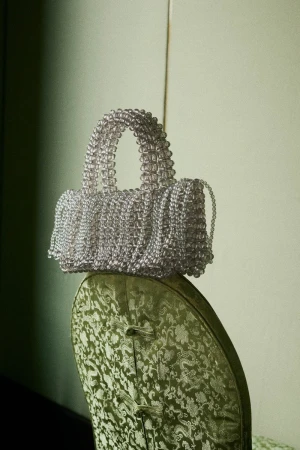 Elegant handbag crafted from translucent beads resting on a vintage chair with patterned upholstery, creating a sophisticated visual.