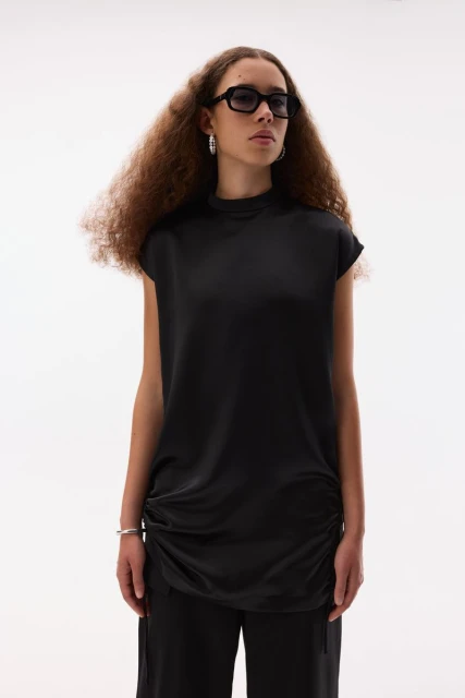 Fashion portrait of a woman with curly hair wearing black top and pants in a minimalist studio setting with soft, even lighting.