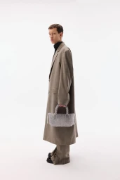 Model wearing a long brown coat and holding a beaded handbag against a seamless white background
