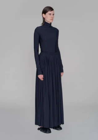 Model Jamily Wernke Meurer wearing a navy turtleneck and pleated maxi skirt against a grey backdrop.