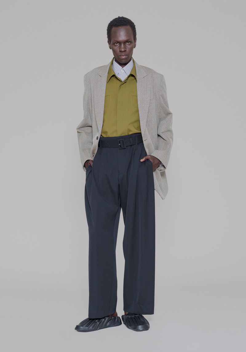 Marwang Lual in an oversized grey blazer, olive shirt, and wide-leg black trousers against a neutral studio backdrop.