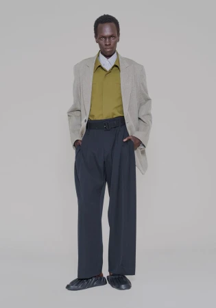 Marwang Lual in an oversized grey blazer, olive shirt, and wide-leg black trousers against a neutral studio backdrop.