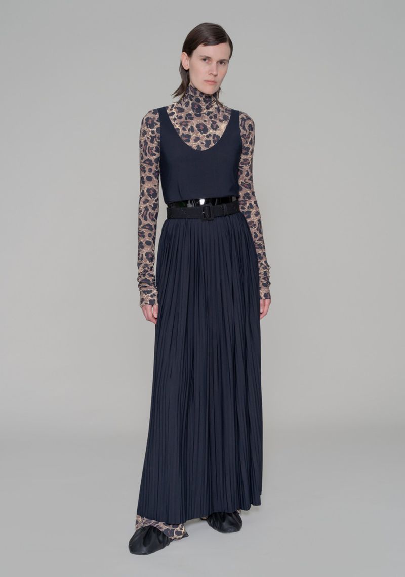Full-length shot of a fashion model posing in a sleeveless top, pleated skirt with a belt, and a long-sleeved animal print top and pants.