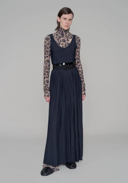 Full-length shot of a fashion model posing in a sleeveless top, pleated skirt with a belt, and a long-sleeved animal print top and pants.