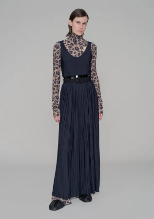 Full-length shot of a fashion model posing in a sleeveless top, pleated skirt with a belt, and a long-sleeved animal print top and pants.