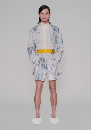 Model standing against a studio backdrop wearing an Overcoat New York botanical print jacket, matching shorts, and a yellow waistband.