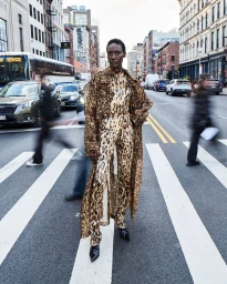 Model wearing a leopard print coat and matching pants standing on a city crosswalk with blurred traffic