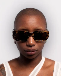 Close-up portrait of a bald person wearing tortoiseshell sunglasses against a white background