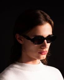 Close-up portrait of a person wearing black sunglasses and a white knitted sweater against a dark background.