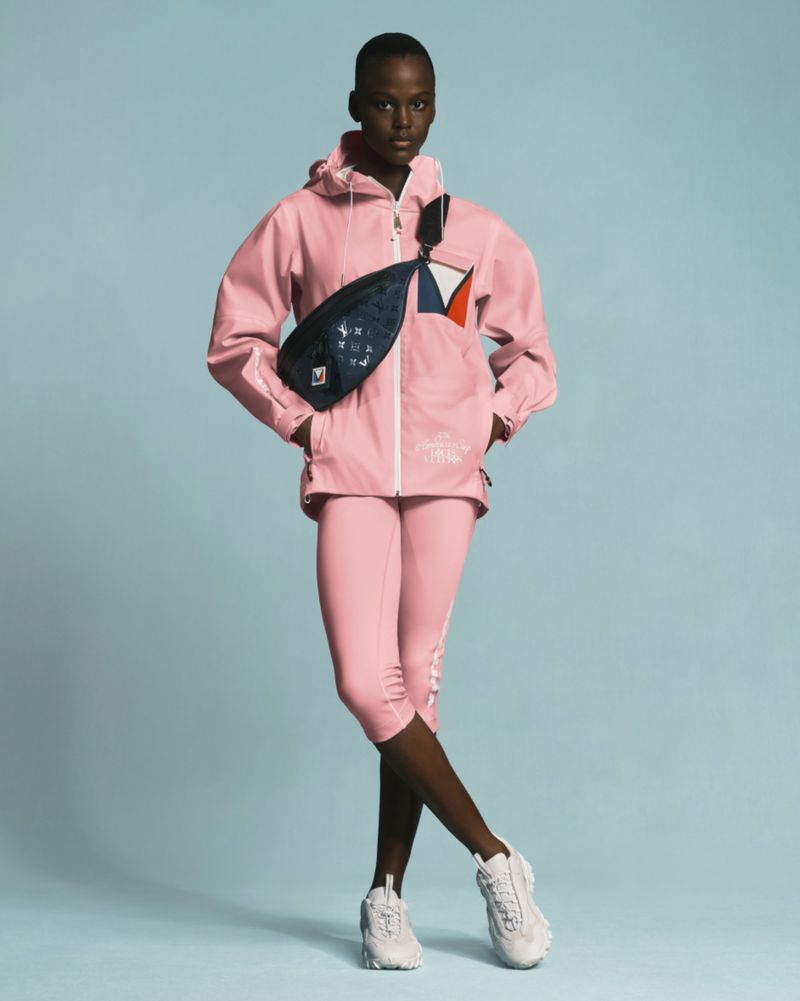 Full body shot of African American fashion model in pink jacket and leggings against a blue studio background, with a branded fanny pack.