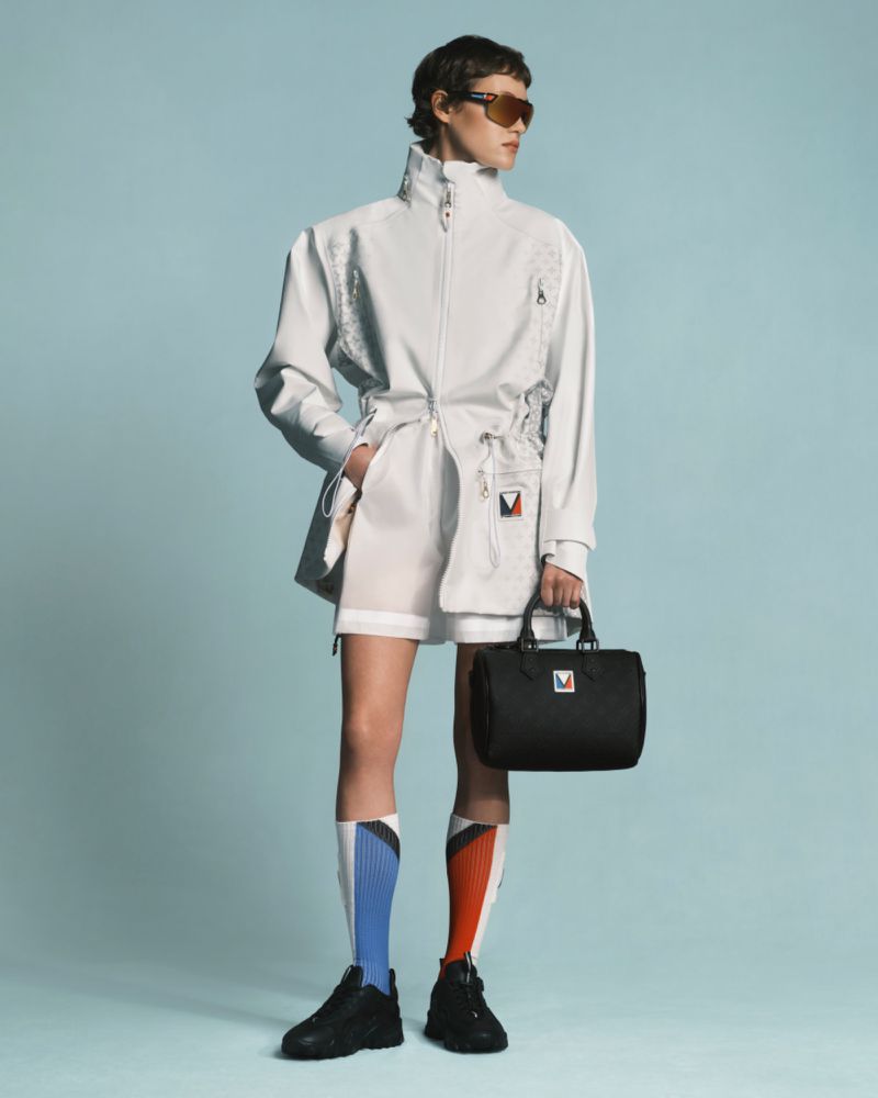 Fashion shot featuring a person in a white track suit and black shoes holding a black bag against a light blue background.