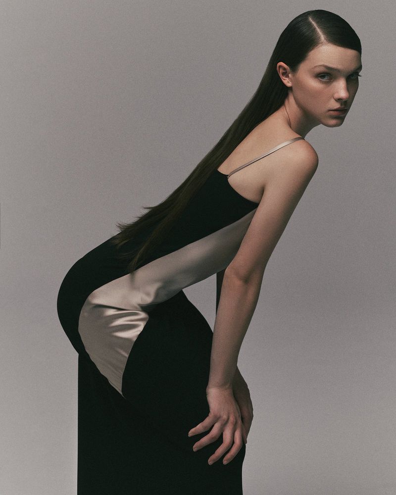 Model posing in a black and champagne two-tone satin slip dress against a smooth grey seamless studio background.