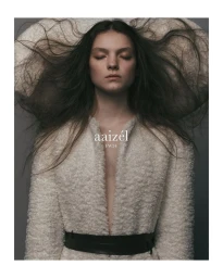 Model with eyes closed and hair fanned out wearing a cream textured coat with a black belt for Aaizél FW24.