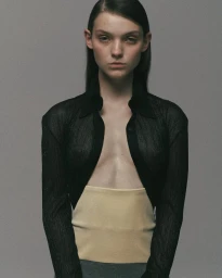 Model in unbuttoned black shirt and beige bandeau against a grey background for Aaizel FW24