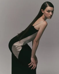 Model posing in a black and champagne two-tone satin slip dress against a smooth grey seamless studio background.