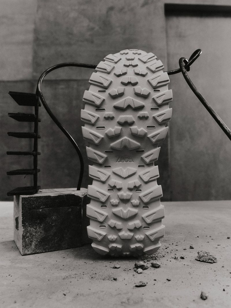 Detailed view of a shoe sole revealing its intricate tread pattern, placed on a stone surface, set against a textured grey backdrop.